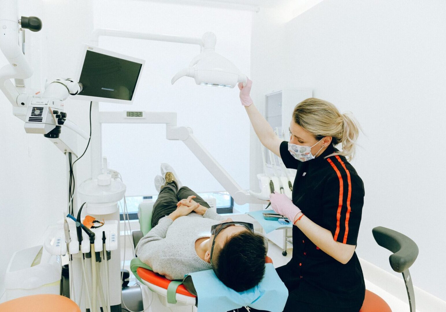 A woman is standing over a man in the dentist 's chair.