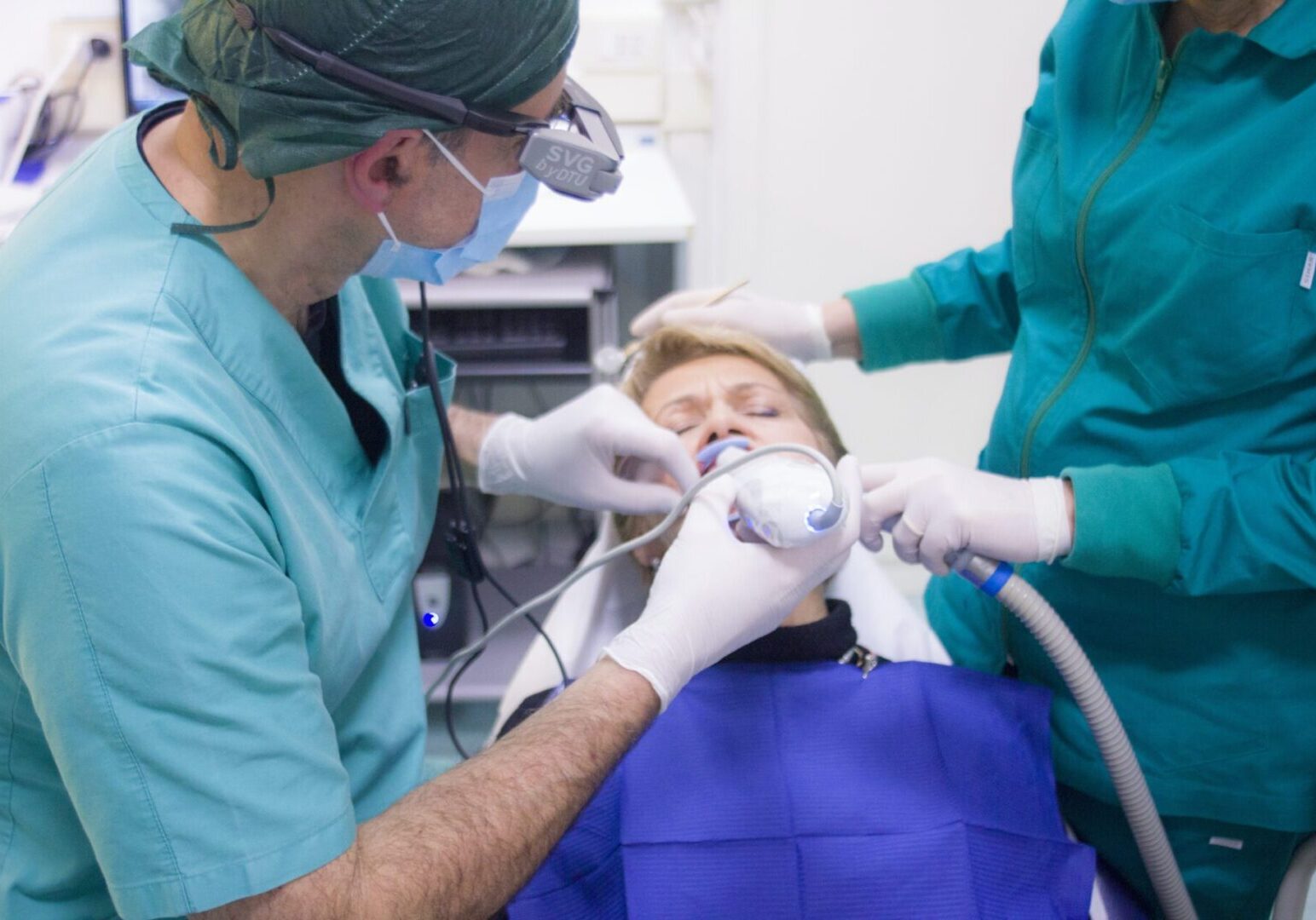 A dentist is using an electric toothbrush to clean the teeth of another person.